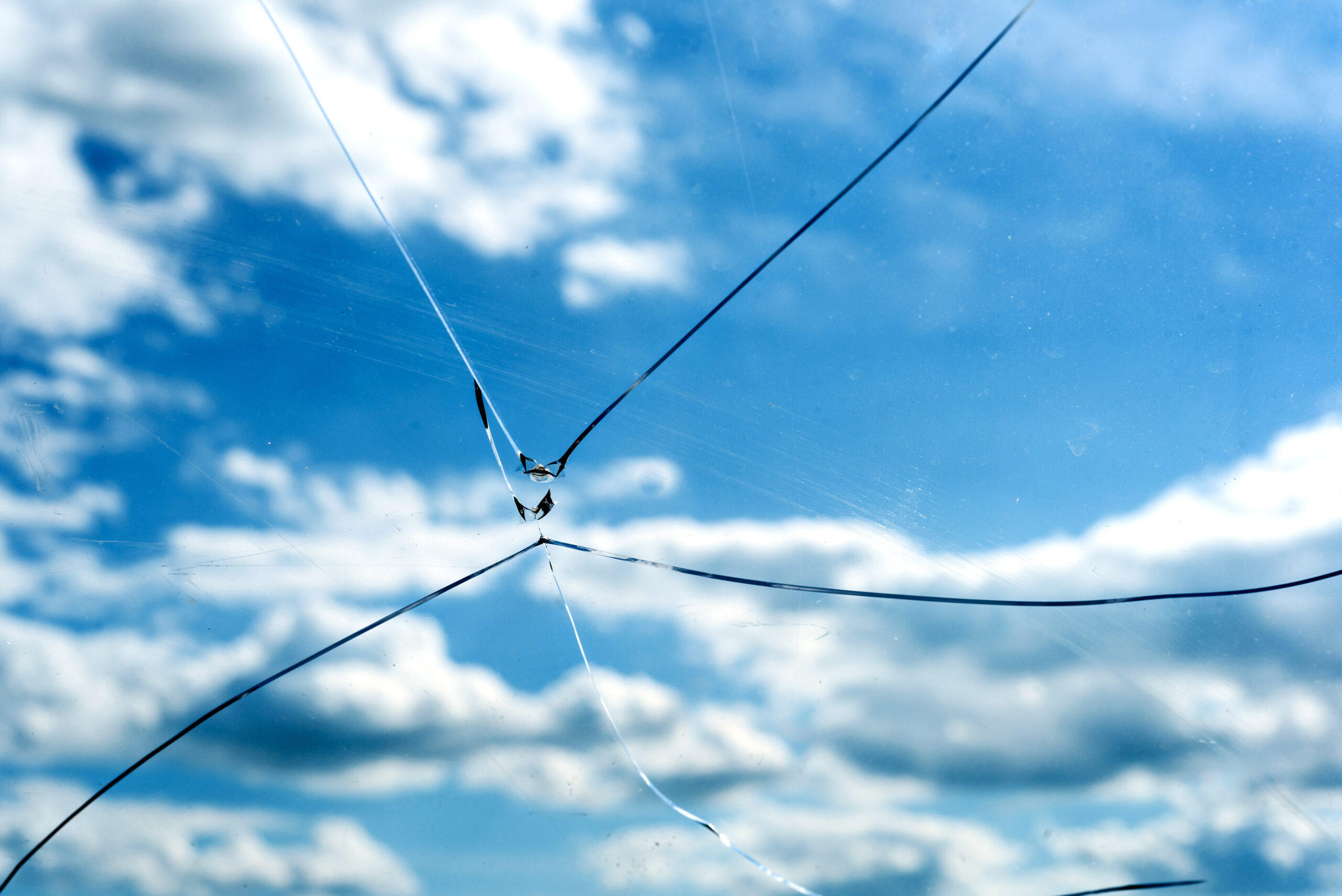 Single accurate cracked glass window with a blue sky background and white summer clouds